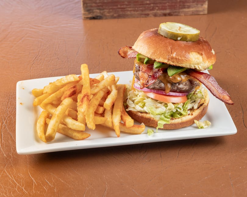 A bacon cheeseburger with lettuce, tomato, onion, avocado, and a pickle, served with fries.