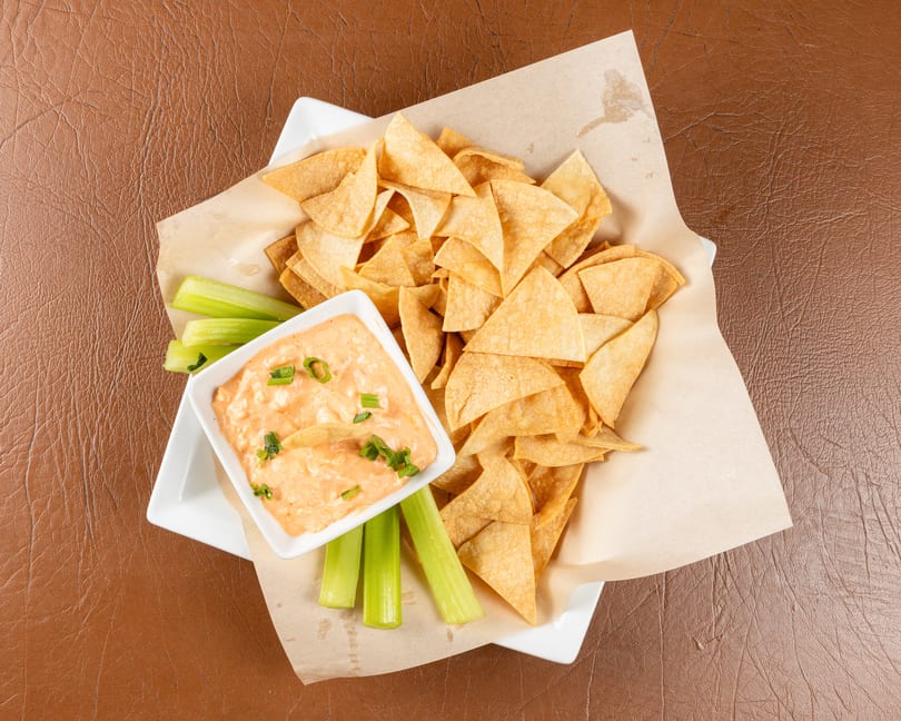 Top-down view of a white plate with tortilla chips, celery sticks, and a bowl of dip.