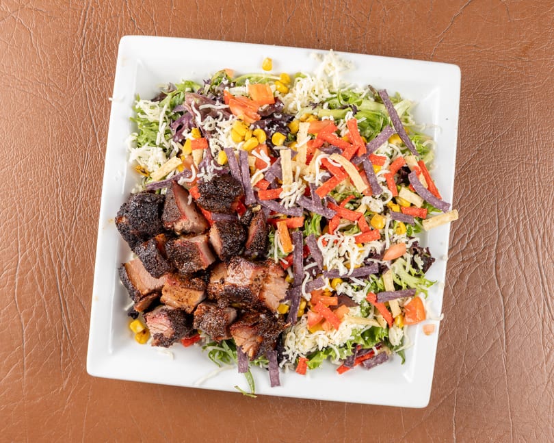 Overhead view of a white plate with chopped brisket and a colorful salad with cheese and tortilla strips.