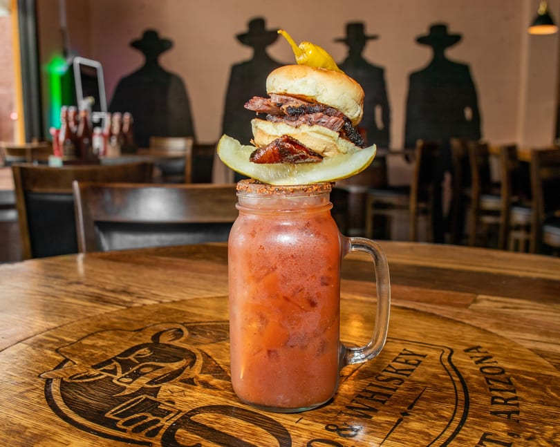 A Bloody Mary in a mason jar, topped with a brisket slider, pickle, and pepper.