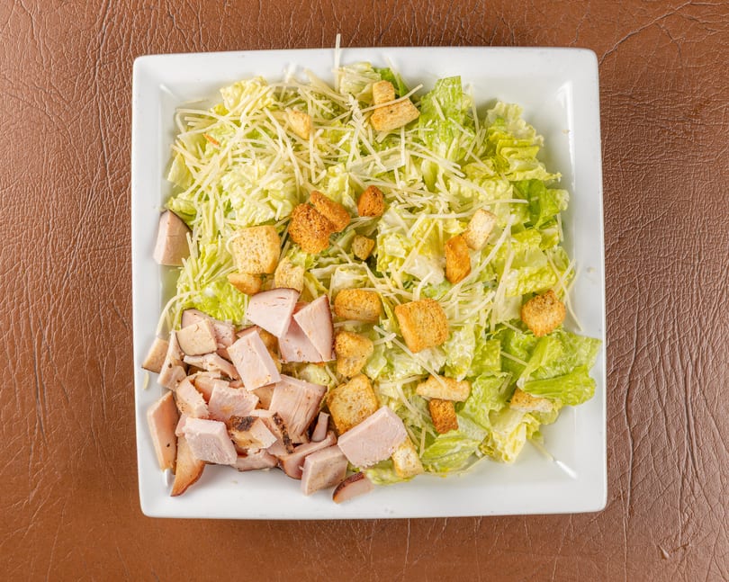 Overhead view of a Caesar salad with chicken, croutons, and shredded cheese on a white rectangular plate.
