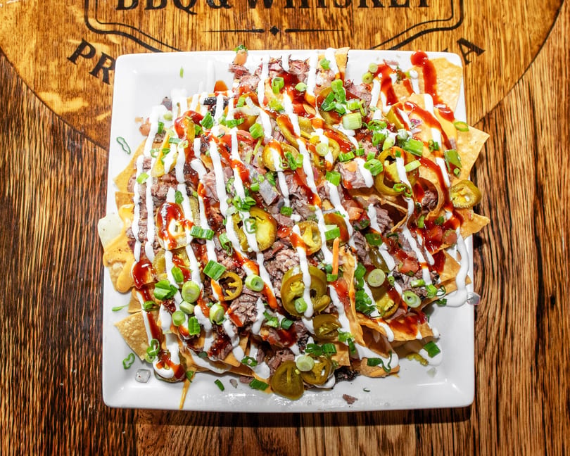 Loaded nachos with meat, jalapeños, green onions, and sauces on a white plate.